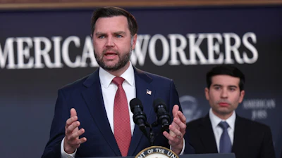 Man in navy suit speaking at podium with Presidential Seal, addressing audience at American Workers event