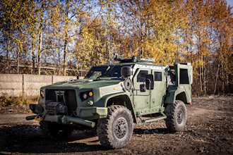 Tactical armored military vehicle with open door parked outdoors against autumn trees