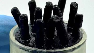 Black rod-like structures in clear cylindrical container against blue background