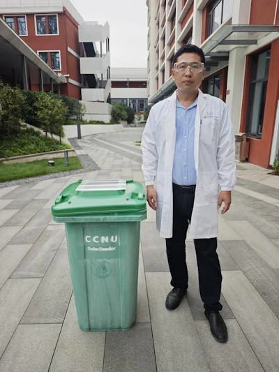 Man in white lab coat standing beside green CCNU waste bin on university campus courtyard