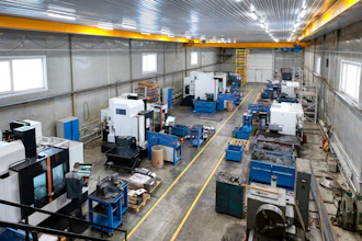 Industrial manufacturing facility with CNC machines, blue workbenches, and overhead yellow crane system in warehouse space