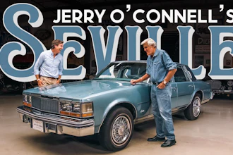 Jerry O'Connell and a man examine a blue classic Oldsmobile Cutlass in a showroom