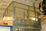 Industrial safety cage with mesh panels and yellow-black striping in warehouse facility