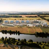 Aerial view of industrial facility with blue-roofed buildings, storage tanks, and surrounding agricultural fields near a river