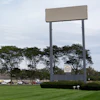 Large blank billboard with metal frame in commercial area surrounded by trees, buildings, and parked vehicles