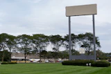 Large blank billboard with metal frame in commercial area surrounded by trees, buildings, and parked vehicles