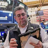 Trader at NYSE trading floor wearing headset and holding tablet with monitors displaying market data and American flag in background
