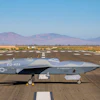 Gray RQ-4 Global Hawk military drone aircraft parked on desert runway with mountains in background