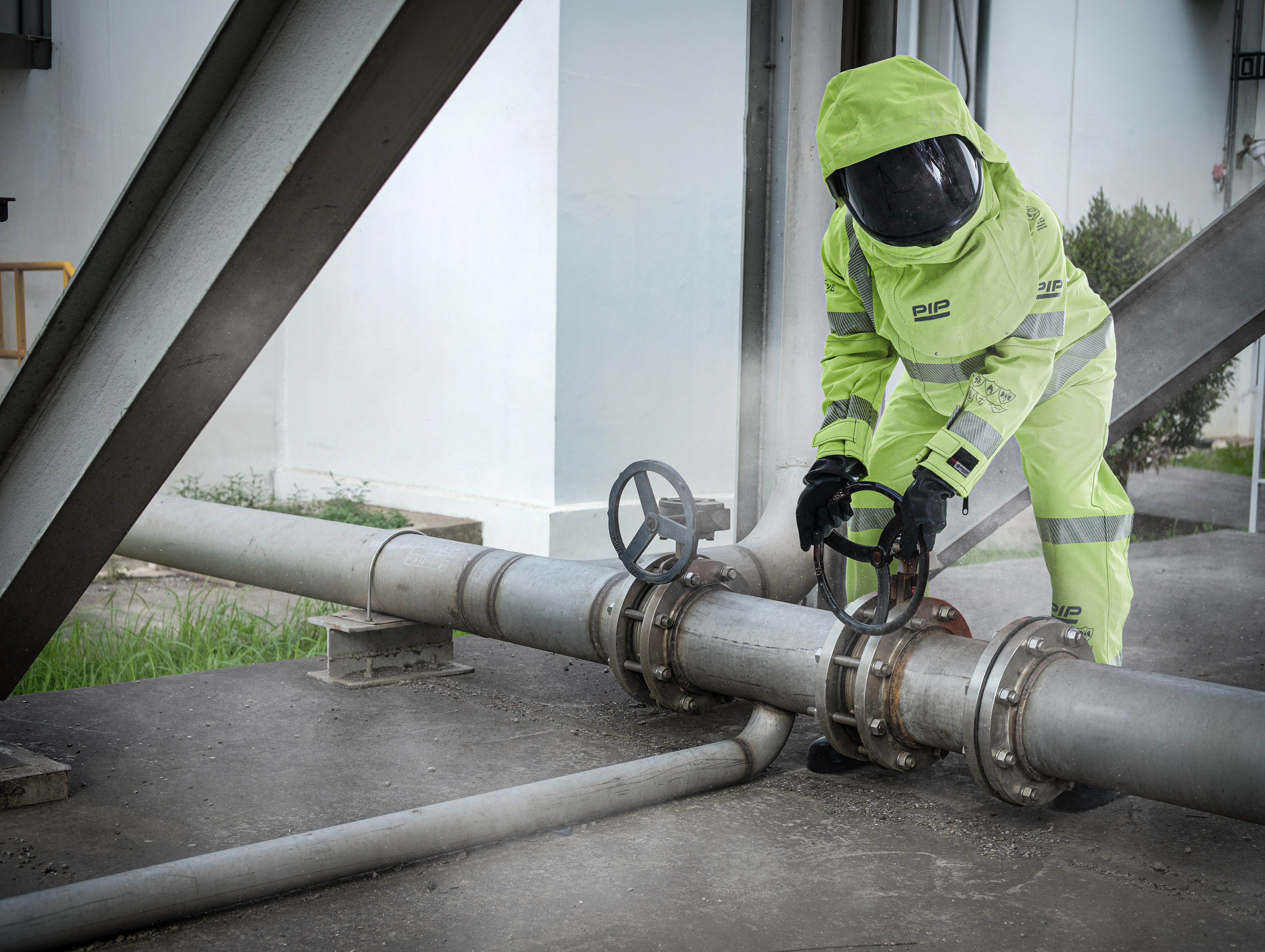 Industrial worker in neon safety gear adjusting valve on large metal pipeline system