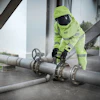 Industrial worker in neon safety gear adjusting valve on large metal pipeline system