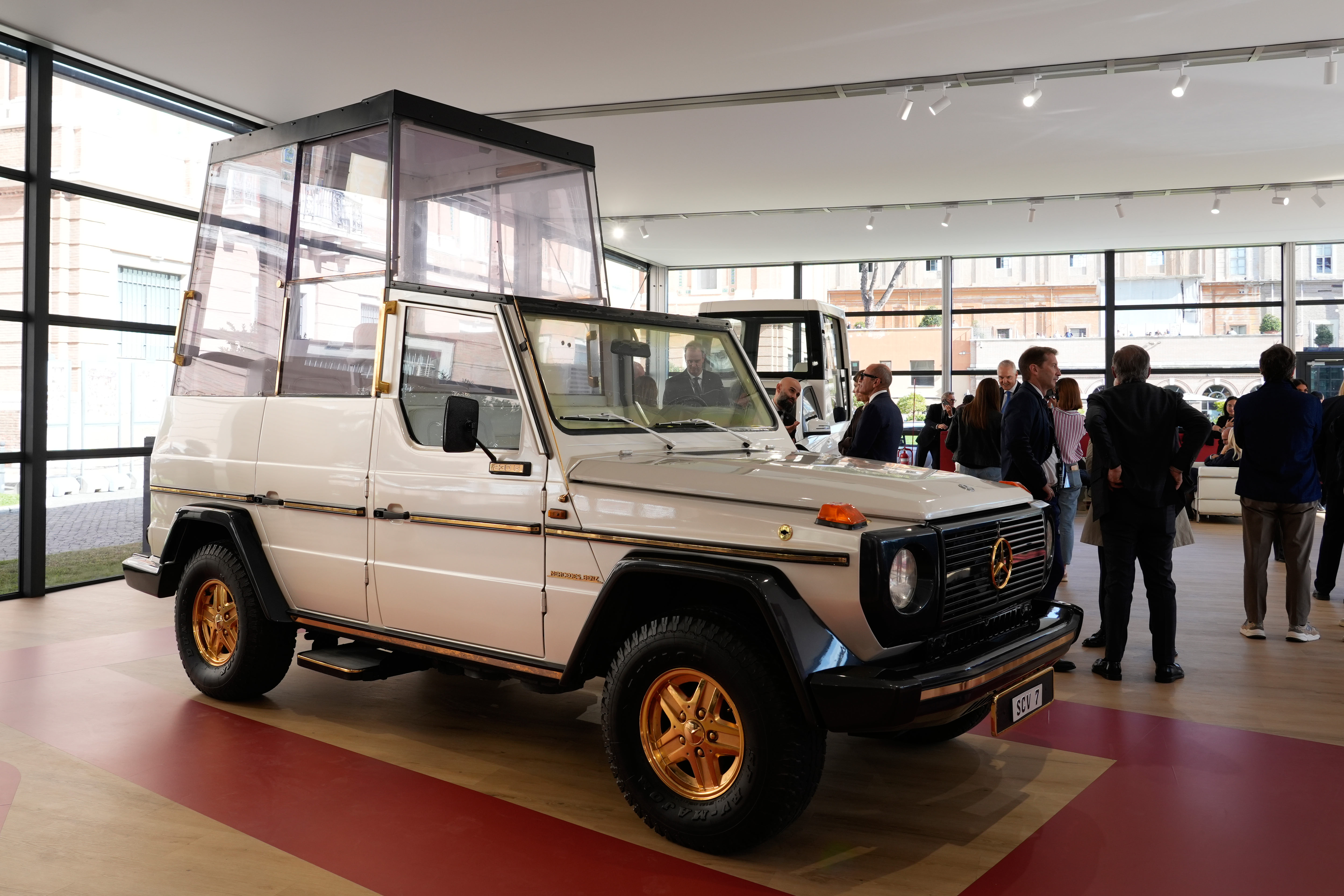 Vintage Mercedes-Benz G-Class with white body and gold wheels displayed in modern showroom with visitors