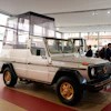 Vintage Mercedes-Benz G-Class with white body and gold wheels displayed in modern showroom with visitors