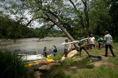 Community members assist with river rescue operations near a large tree on muddy riverbank