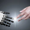Human hand reaching toward robotic hand in a gesture of connection and collaboration against a gray background with light rays
