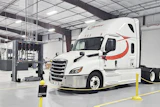 White Schneider semi-truck with red stripe parked in industrial warehouse facility with yellow safety barriers