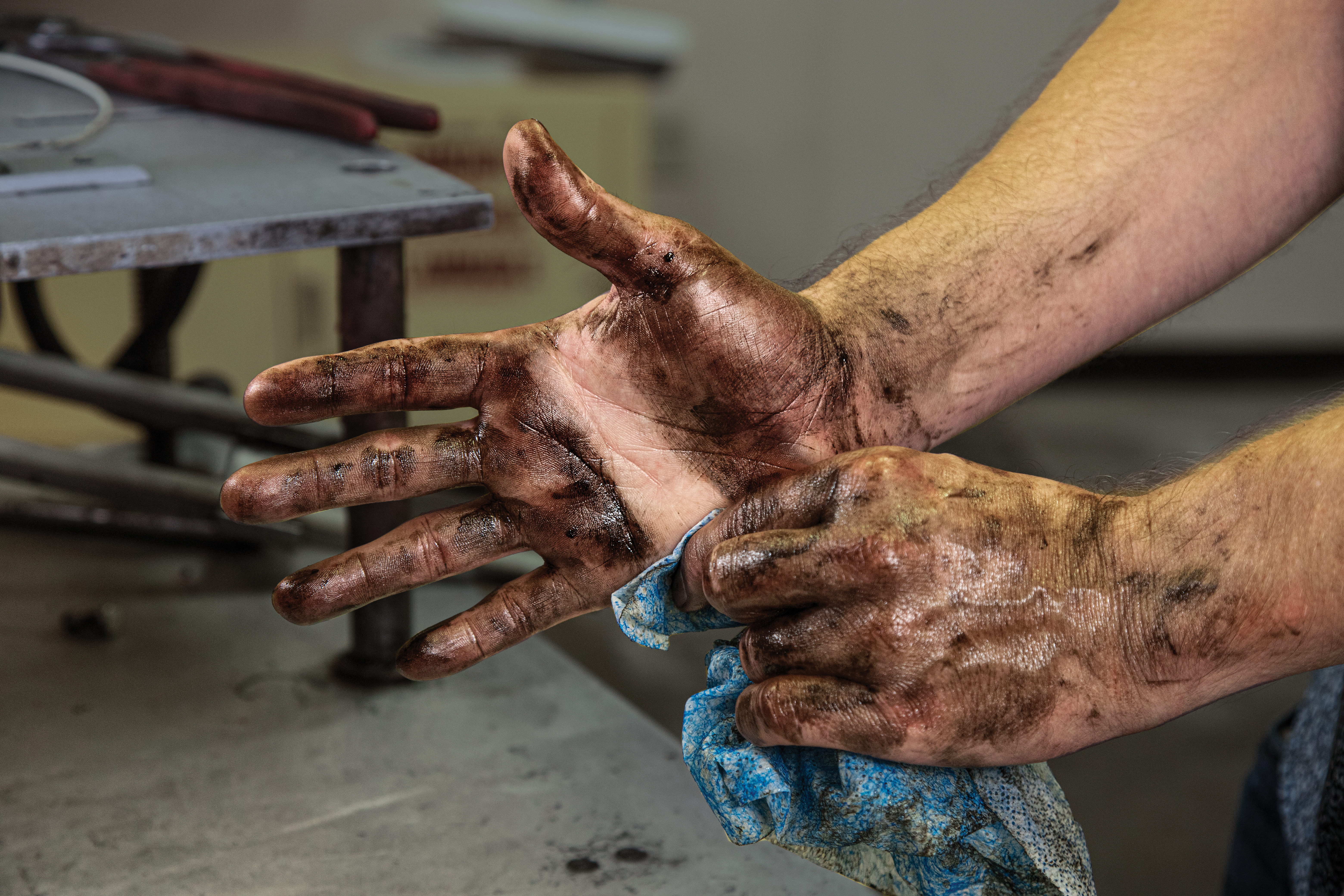 Two dirt-covered hands showing calluses and wear from manual labor in a workshop setting