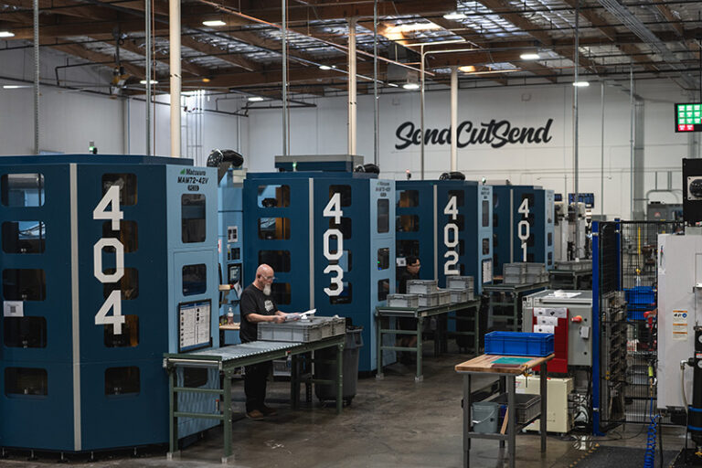 Industrial manufacturing facility with blue CNC machines and Sena CutSend signage on warehouse wall