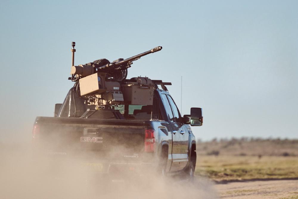 Military-equipped GMC pickup truck driving through dusty desert terrain