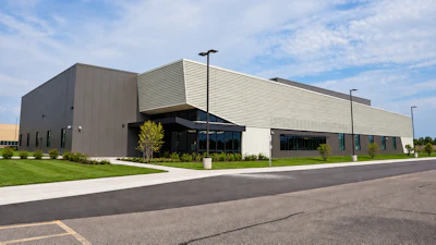 Modern industrial building with metal siding, glass entrance, and manicured landscaping under blue sky