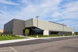 Modern industrial building with metal siding, glass entrance, and manicured landscaping under blue sky