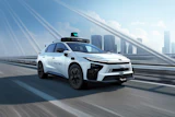 White autonomous taxi vehicle with blue accents driving on elevated highway with city skyline in background