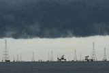 Offshore oil and gas extraction platform with multiple derricks and pump jacks silhouetted against dark storm clouds