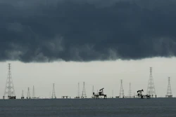 Offshore oil and gas extraction platform with multiple derricks and pump jacks silhouetted against dark storm clouds