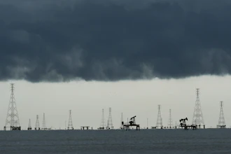Offshore oil and gas extraction platform with multiple derricks and pump jacks silhouetted against dark storm clouds