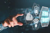 Hand reaching toward glowing hexagonal security icons with Zero Trust text in teal and blue digital interface