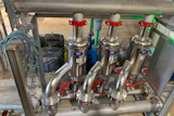 Industrial stainless steel multi-valve manifold system with red handles mounted on frame in workshop